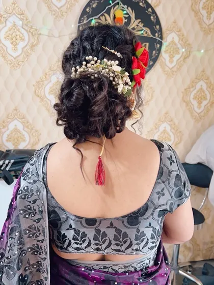 A modern messy bun hairstyle, perfect for a reception or sangeet. It is decorated with a combination of fresh red roses and baby's breath.