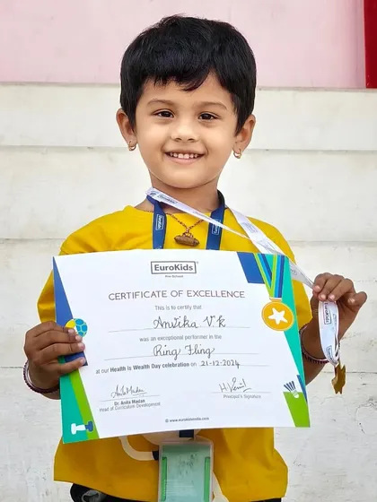 Achievement unlocked. A young girl smiles brightly as she holds her certificate for being an exceptional performer in the 'Ring Fling' game on Health is Wealth Day.