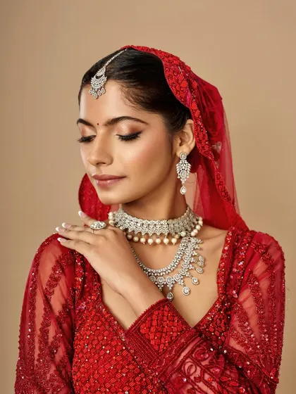 A soft, elegant pose capturing the complete traditional bridal look. The makeup complements the heavy jewelry and red lehenga without overpowering the bride's natural beauty.