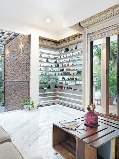 This informal living area on an upper floor overlooks the courtyard through a glass railing. The design features a corner display for artifacts and large sliding doors that open to a terrace, enhancing the connection to the outdoors.