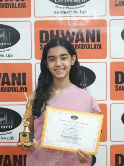 A student in a beautiful pink saree holds her award.