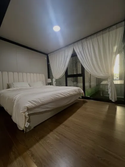 A bedroom in one of our container homes, designed for peace and comfort. The combination of wood flooring, soft lighting, and large windows creates a serene personal retreat.