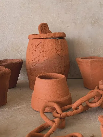 Another view of the raw terracotta pieces, including a pot with a delicate chain and a lidded jar with leaf carvings.