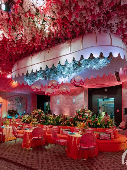 The evening look of our 'La Dolce Vita' theme, where the space was transformed with dramatic pink lighting. A custom canopy filled with blue hydrangeas became a central feature, surrounded by plush orange seating and tables set for a luxurious dinner.