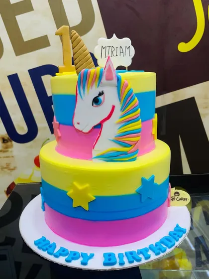 A vibrant 4kg two-tiered unicorn cake with a rainbow-maned unicorn head and colorful striped tiers.