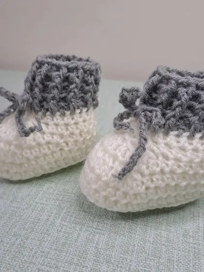 These unisex baby booties in grey and white are a modern and versatile choice, with a fold-over cuff and tie closure.