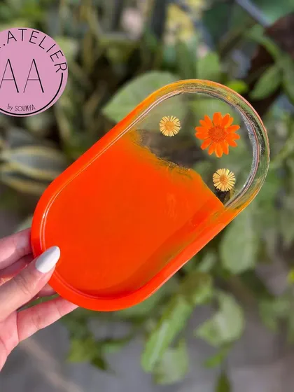 An oval trinket tray in a sunny orange hue, decorated with delicate dried flowers. It's a simple yet beautiful way to keep your small items organized.
