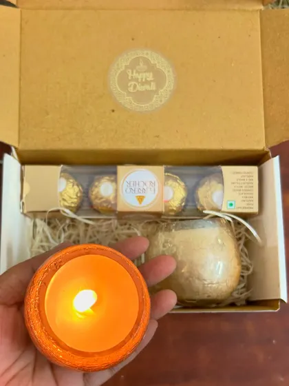 Holding one of the lit candles from the mini Diwali hamper. The orange wax gives off a warm, festive glow.