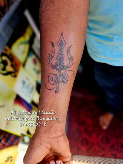 A finished Trishul and Damaru tattoo on the forearm, a classic symbol of Shiva's power.