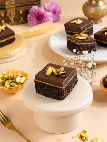 Rich chocolate and pistachio mini cakes, beautifully arranged on pedestals to give them a gourmet, artisanal feel.