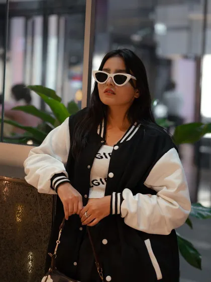 A stylish portrait of a model in a varsity jacket, leaning against a window. The reflection and the indoor plants add layers to this cool, urban shot.