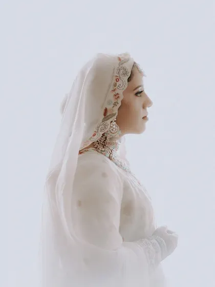A high-key, ethereal side profile of a Muslim bride, emphasizing the delicate details of her headwear and her serene expression.