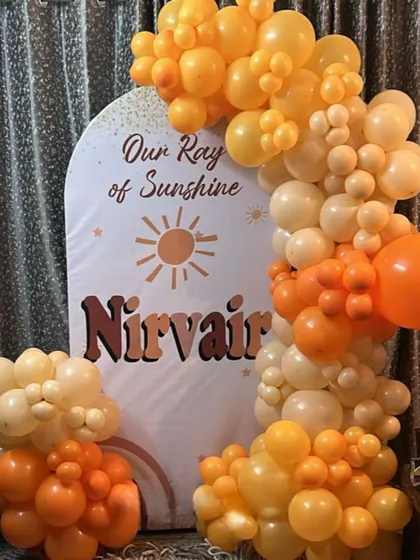 A warm and sunny "Our Ray of Sunshine" themed birthday party. The decor uses a palette of orange and yellow balloons against a custom arched backdrop.