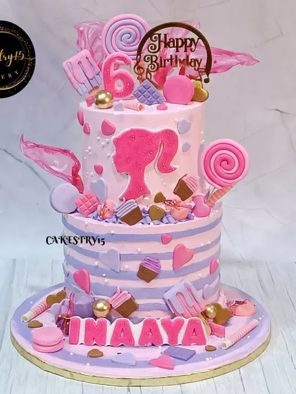 A glamorous two-tier Barbie-themed chocolate cake. Decorated in shades of pink and purple, it features a Barbie silhouette, macarons, and fondant ice candies for a stylish 6th birthday.