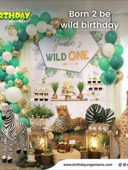 A "Wild One" jungle-themed birthday setup. This elegant design uses a green, white, and gold balloon garland, along with realistic animal props like a zebra, leopard, and giraffe for a sophisticated safari vibe.
