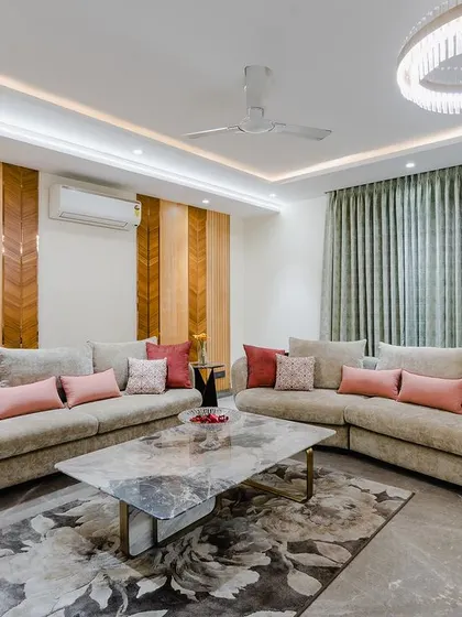 In this spacious drawing room, two large beige sofas face each other, creating an ideal setup for entertaining. The wood-paneled wall adds warmth and texture, while the large chandelier provides a luxurious touch.