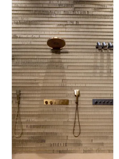 A close-up of a shower system displayed on the corrugated cardboard wall. The raw, tactile quality of the background contrasts beautifully with the sleek, metallic finish of the fixtures.