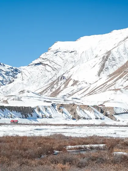 A wide landscape shot of the Spiti Valley, showing the contrast between the snow-covered mountains, the barren brown earth, and the clear blue sky. It's a testament to the raw, unfiltered beauty of the region.