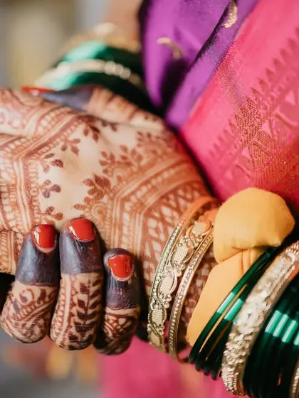 A close-up on the bride's hands, showing her engagement ring, red-tipped fingers, and intricate henna design.