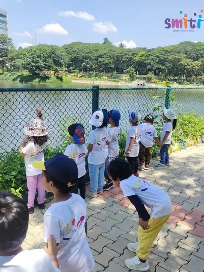 A group of children stands by the fence at Byrasandra Lake, pointing out birds and plants. These trips foster a deep appreciation for the natural world.