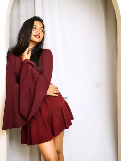 A thoughtful and serene pose, with the model looking away, framed by a white archway that contrasts with her deep red outfit.