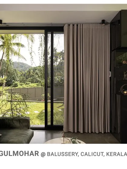The living room at Gulmohar features a floor-to-ceiling glass wall that slides open to the garden, offering expansive views and merging the interior with the lush landscape.