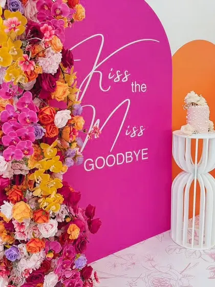 "Kiss the Miss Goodbye" with this bold and colorful backdrop. The vibrant floral arrangements against the hot pink arch create a fun and energetic atmosphere perfect for a bachelorette celebration.