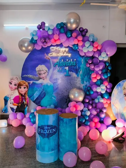 A complete Frozen-themed first birthday backdrop we designed for a magical celebration. This setup includes a custom circular backdrop featuring Elsa, a cascading balloon garland in purple and blue hues, and a large light-up number '1'.