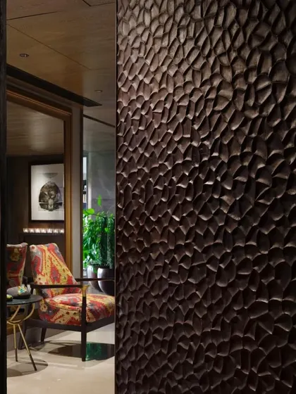 A detail of the hand-scooped teak wood door at the entrance of the Caitriona apartment. The deep, charcoal-black 'Shou Sugi Ban' finish provides a powerful, textural statement.