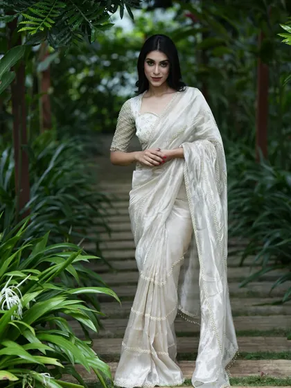 A full-length shot of the white tissue silk saree in a lush green setting, highlighting its serene and elegant appeal.
