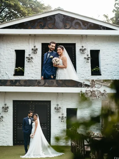 A fairytale-like portrait of the couple outside a charming white building. The setting adds a touch of vintage romance to their modern Catholic wedding.
