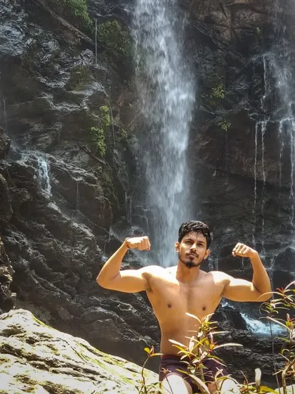 A shirtless pose in front of a waterfall.