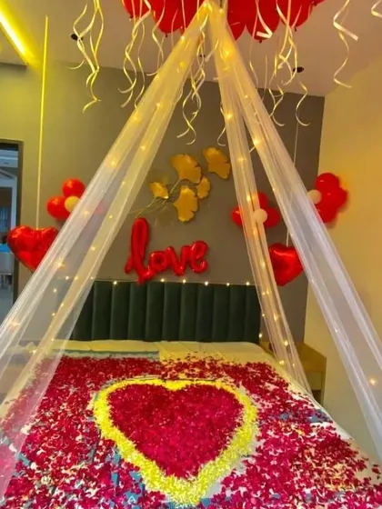 A stunning cabana bed decoration with a heart of yellow and red rose petals, surrounded by red balloons and "love" foil letters.
