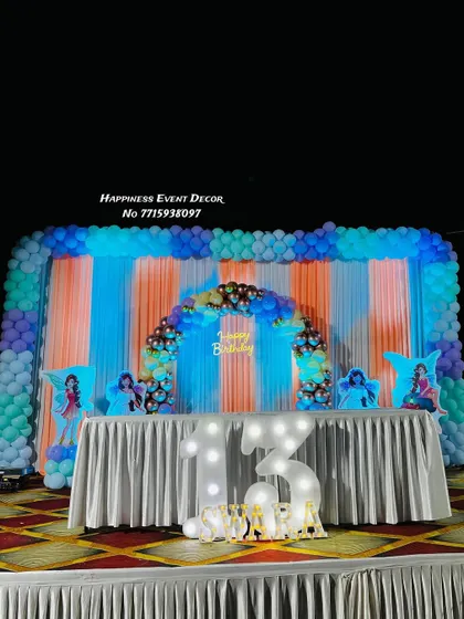 A vibrant setup for a 13th birthday party. The stage is decorated with a large backdrop of colorful curtains and a multi-layered balloon arrangement, perfect for a teenager's celebration.