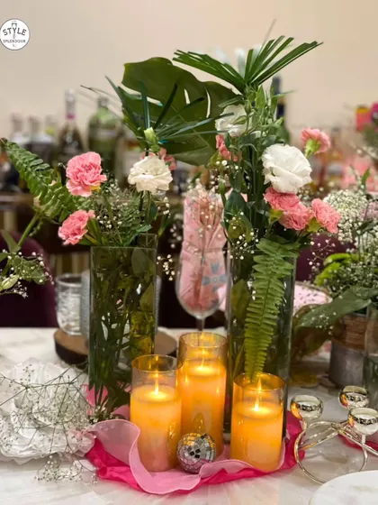 A table adorned with flickering candles and delicate blooms creates an ambiance that warms the heart. This centerpiece combines tall glass vases with pink and white flowers and glowing candles for an enchanting effect.