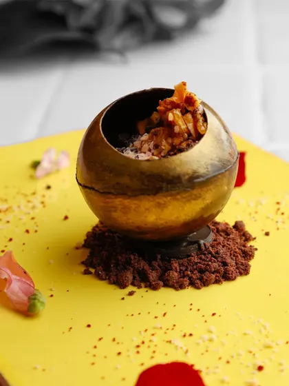 A golden chocolate sphere filled with caramelised mousse and nuts. This dessert combines rich flavours with a playful presentation, inviting guests to crack it open and discover the treasure within.