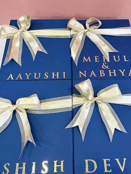 A close-up of the elegant, deep blue groomsmen boxes, featuring custom electroplated names and beautiful satin organza ribbons. The quality of the packaging is just as important as the gifts inside.