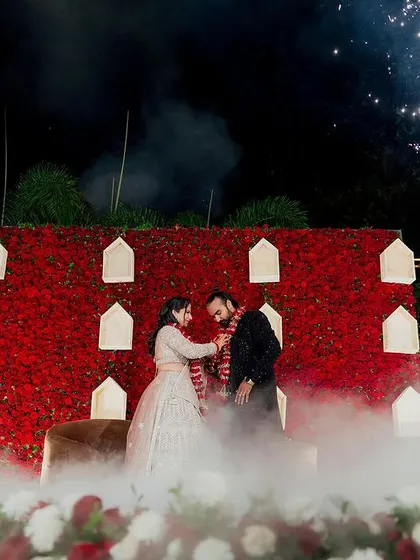 The varmala exchange on the dramatic red floral stage, captured with the full effect of the surrounding sparklers and ethereal fog.