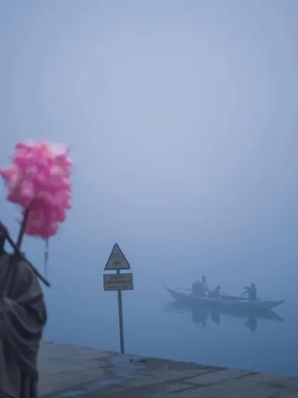 A candy floss seller stands on the foggy ghats, a surreal splash of pink against the muted blue tones of the early morning. This image highlights the unexpected moments of beauty in the city.