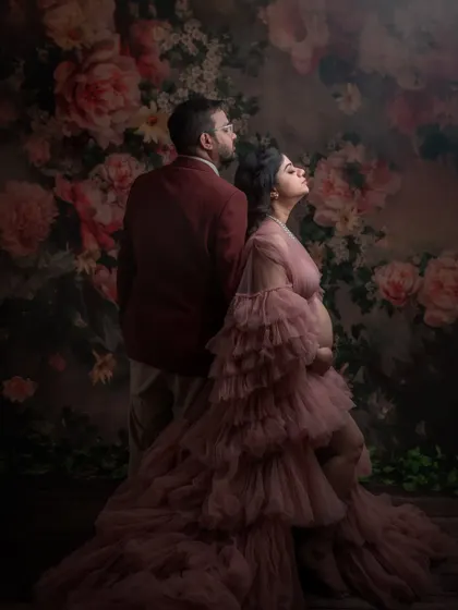 A dramatic and artistic maternity portrait of a couple against a floral backdrop. The moody lighting and the woman's pose create a powerful and romantic image celebrating her pregnancy.