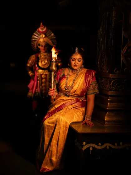 Another shot of Meghana Raj, looking down at the flame. The dramatic lighting highlights her strong features and the traditional attire.