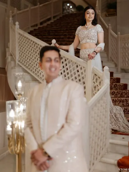 A creative portrait using depth of field, with the groom in the foreground and the bride descending a grand staircase in the background.