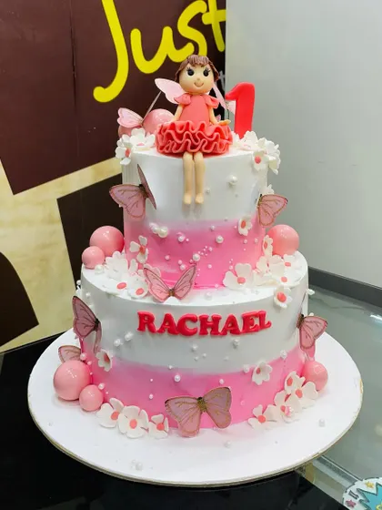 A beautiful 4kg two-tiered cake for a first birthday, featuring a pink ombre design, butterflies, and a sweet fairy topper.