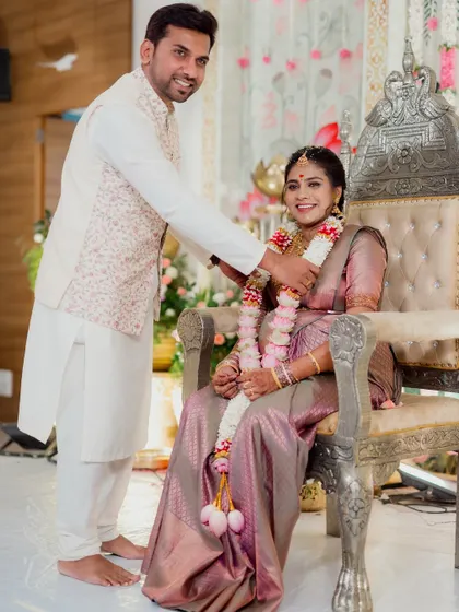 A heartwarming moment from a baby shower or half-saree ceremony, with the couple seated on ornate silver thrones.