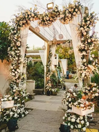 This beautiful wedding entrance features a wooden arch covered in white flowers and greenery. The natural textures and soft colors create a bohemian and elegant vibe.