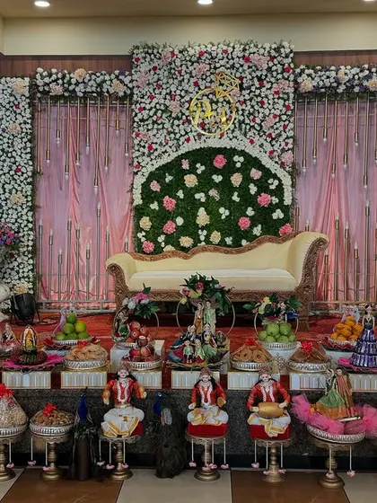 A full view of an engagement platter setup. The display is arranged symmetrically in front of the main seating, featuring couple dolls, peacock motifs, and decorated sweet and fruit trays.