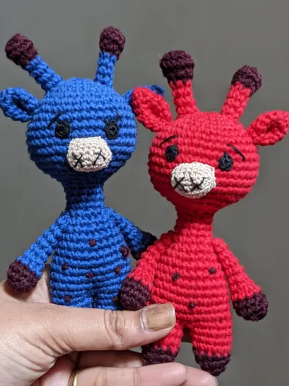 Holding up the red and blue giraffe toys to show them as a pair.