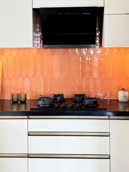 The vibrant orange backsplash provides a stunning backdrop for the black hob and countertop, creating a high-contrast, modern look.