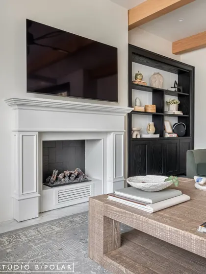 The feature wall of the living room is anchored by a classic white fireplace, creating a traditional focal point. Flanked by built-in display units, the design feels balanced, grand, and inviting.