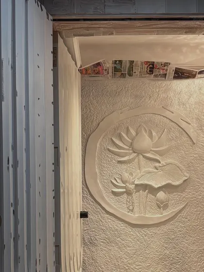 A beautiful white lotus mural installed in an entryway, creating a serene and welcoming first impression. The piece is sculpted on a textured background within a crescent moon shape.